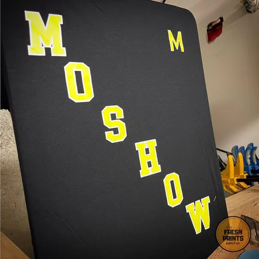 Black garment with MOSHOW in large yellow block letters running diagonally