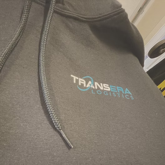Grey hoodie with the TransEra Logistics logo embroidered in teal and white