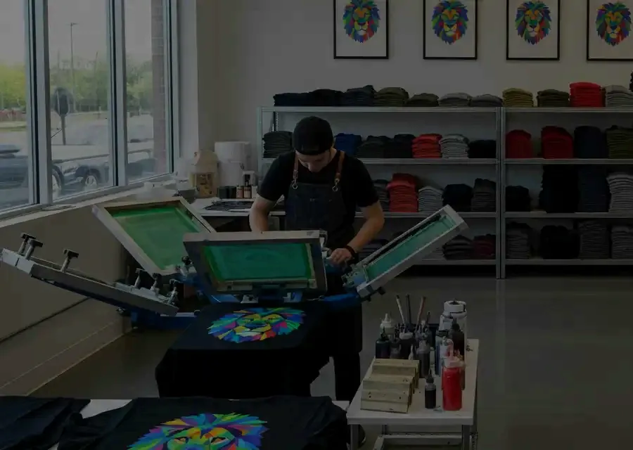 Our printer working a screen printing press with finished lion-design shirts in the Surrey shop